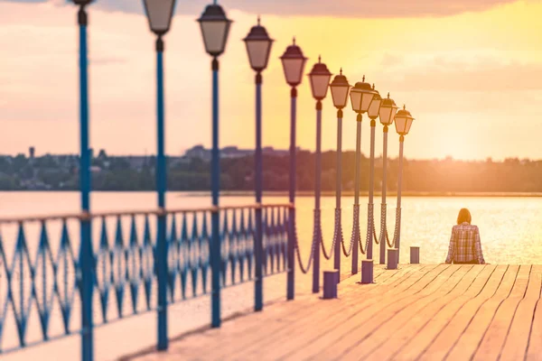 Young woman sitting on pier at sunset — Stock Photo, Image