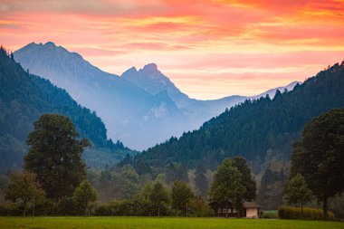 Bavyera 'daki dağlar, Almanya, Avrupa. Ön planda çayır ve arka planda bulutlu gökyüzü ile gün batımı sahnesi