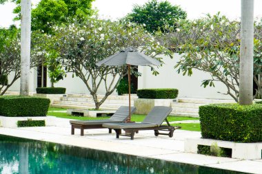 Yüzme havuzunun yanında güneş banyosu kanepeleri büyük şemsiyeli ve arka planda ağaçlar