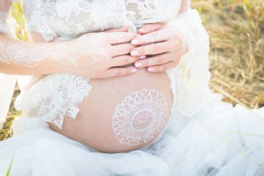 Beyaz elbiseyle hamile karnı boyamak, çimlerin üzerinde açık hava fotoğrafçılığı.