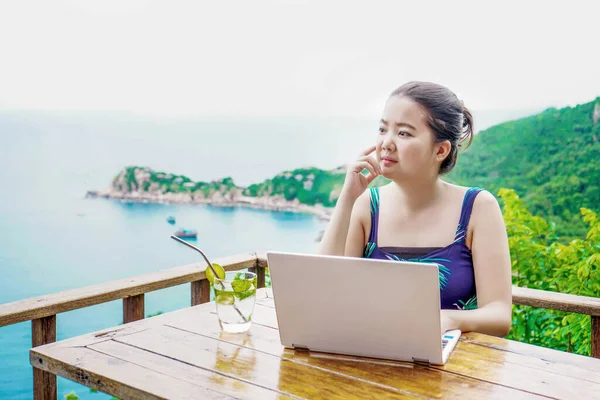 Asian young lady working online happily with background of sea view from balcony above sea level height