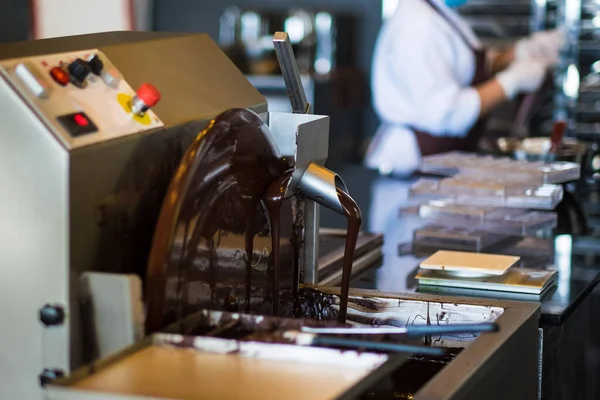 Chocolate making machine operating with blurry background of kitchen staff