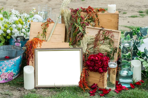 Empty photograph frame on grass with other rustic decoration, flower, wooden boxes, vases, candles, etc