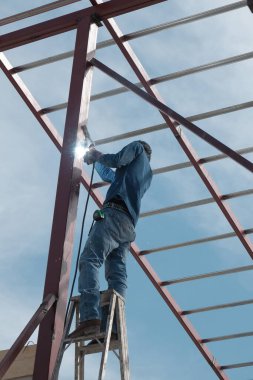 Korunmasız amatör inşaat işçisi merdivende çelik kaynak çubuğu, evin çatısında çalışıyor.