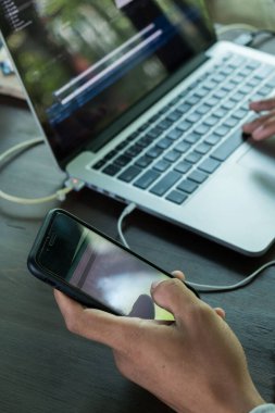 Görünürde logo ya da marka yok. Bilgisayarın arka planında cep telefonu kullanan el resmi