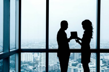 Pencerenin kenarındaki işi tartışan iki ofis çalışanının silueti.