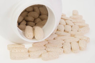 Çeşitli ilaç hapları, beyaz plastik şişeden dökülen haplar.