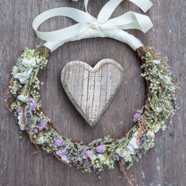 Tahta kalp çiçek buketi ile ahşap arka planda çiçek tacıyla çevrili. natürmort