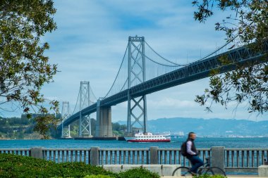San Francisco Bay bridge with blurry man riding bicycle during day time clipart