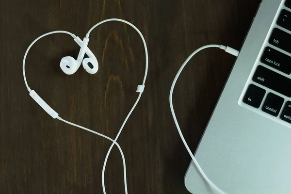 White earphone in heart shape on wooden table by laptop