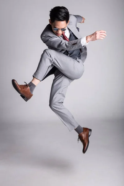 Young Asian business man in suit jumping kick pose. studio photography