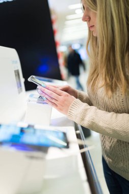 Güzel kadının alışveriş atış kapatın. O mobil olarak ayakta ve dükkanı ve seçimi bir sonraki model onun için tablet. Seçici odak üstünde el.