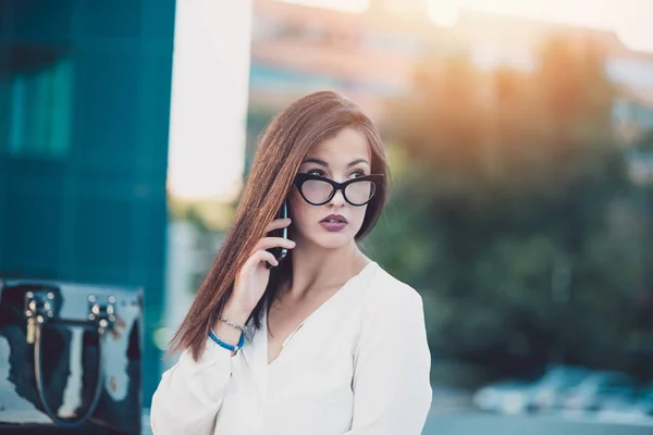 在户外谈话在电话与现代建筑为背景的商业女人肖像 — 图库照片