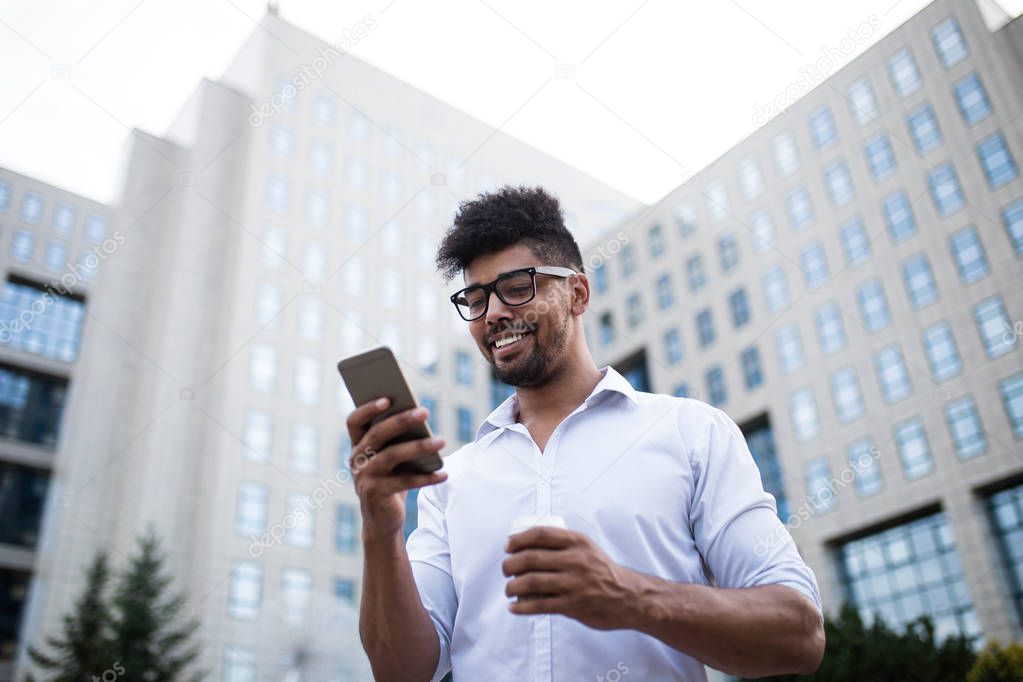 Young handsome Afro American man standing in front of huge modern business building, smiling and talking on mobile phone. 