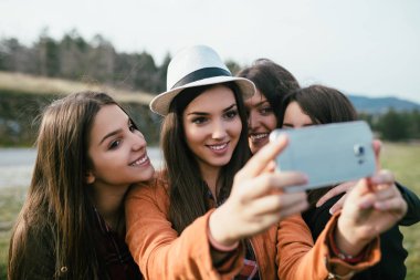 Dört genç kız açık havada eğleniyor ve cep telefonuyla selfie çekiyor