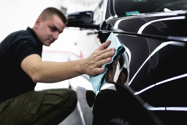 A man cleaning car with microfiber cloth, car detailing (or valeting) concept. Selective focus.