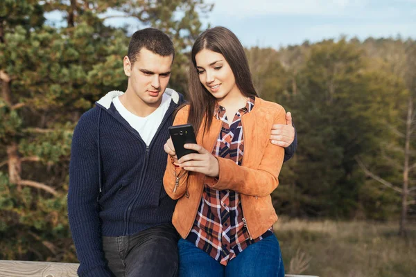Genç çift doğada birlikte eğleniyor ve cep telefonuyla seyahat yerleri arıyor..