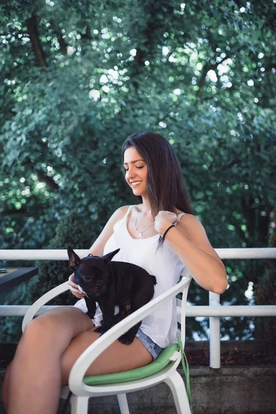 Genç bir kadın kafeteryada eğleniyor ve sevimli bir Fransız buldog yavrusu besliyor. 