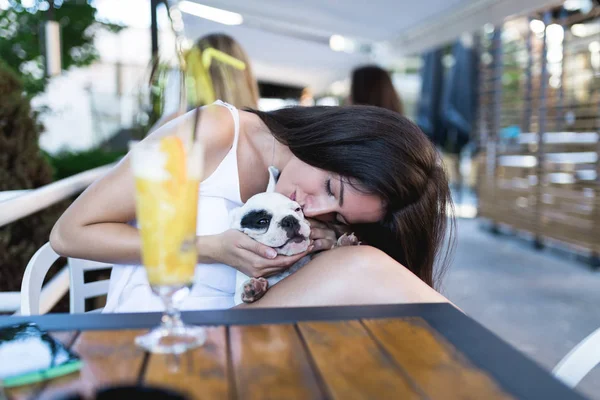 Genç bir kadın kafeteryada eğleniyor ve sevimli bir Fransız buldog yavrusu besliyor. 