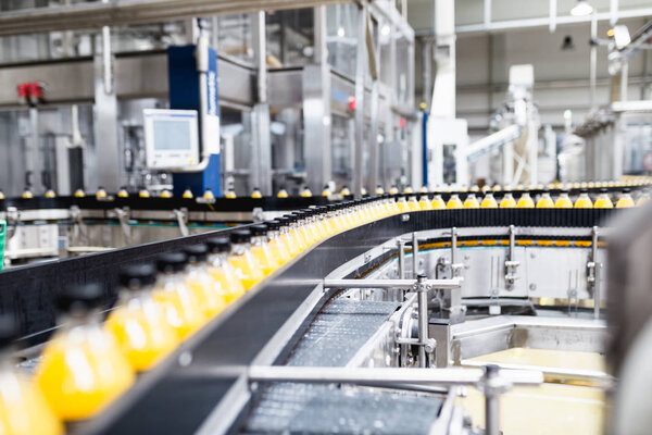 Industrial factory indoors and machinery. Robotic factory line for processing and bottling of soda and orange juice bottles.