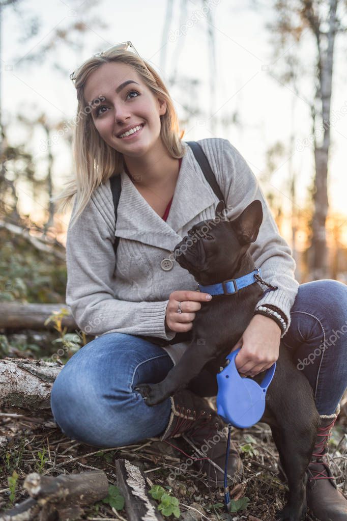 Young  woman holding her french bulldog puppy and enjoying in sunny day. 