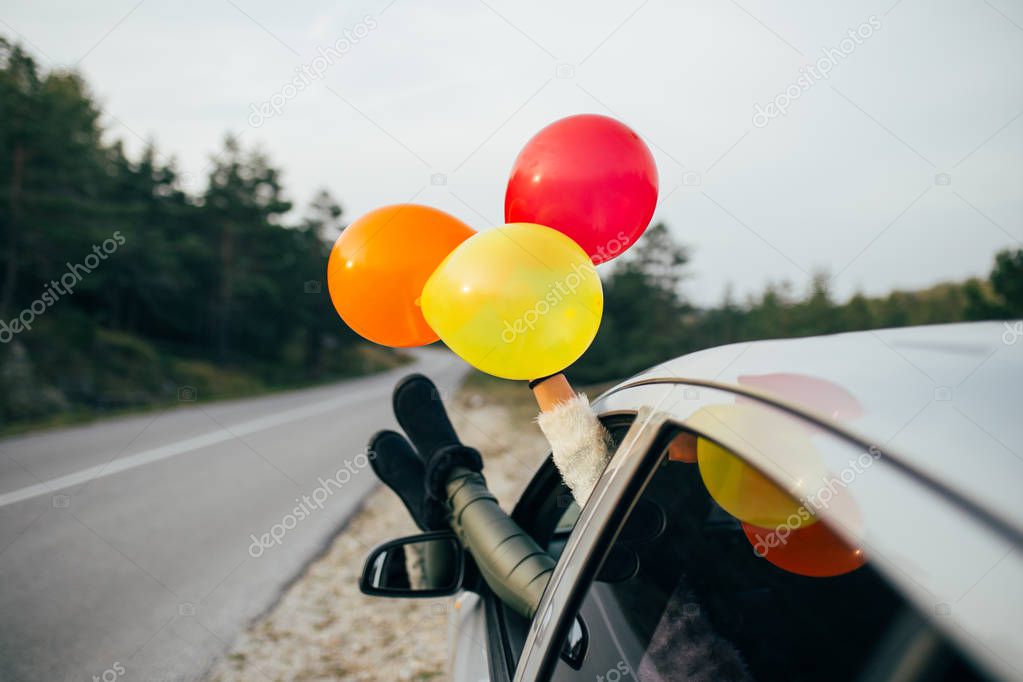 Young woman having fun while holding balloons through car window. Selective focus on woman's hand.