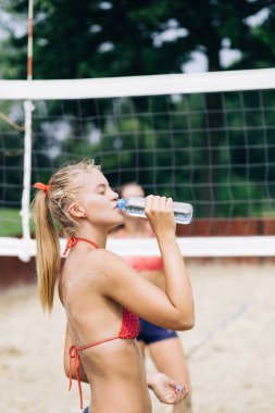 Genç bir kadın sahilde su içiyor. 