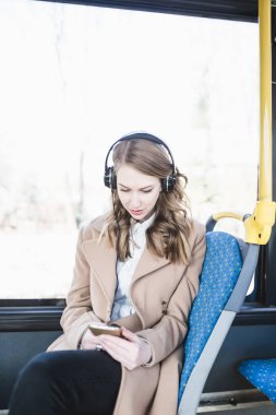 Şehir otobüs içinde oturan, cep telefonu seyir ve müzik güzel mutlu genç kadın.  