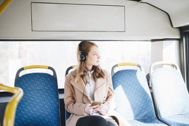 Şehir otobüs içinde oturan, cep telefonu seyir ve müzik güzel mutlu genç kadın.  