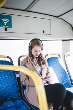 Şehir otobüs içinde oturan, cep telefonu seyir ve müzik güzel mutlu genç kadın. 