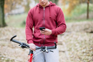 Sonbahar açık havada. Bisiklet Park ile ayakta, cep telefonu tutan kulaklık ile genç ciddi yakışıklı adam. Seçici odak.