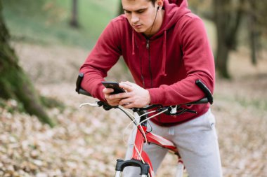 Sonbahar açık havada. Bisiklet Park ile ayakta, cep telefonu tutan kulaklık ile genç ciddi yakışıklı adam. Seçici odak.