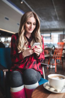 Kafe restoranda oturan, akıllı telefon arayan ve bir kahve içme güzel ve genç birbayan. Ellerinde seçici odak.