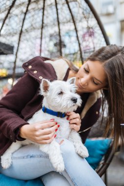 Güzel genç kadın sevimli westie köpek yavrusu ile kafeteryada zevk.