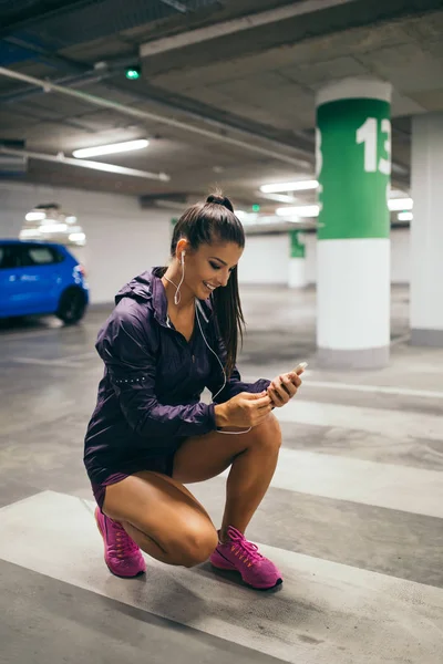 Beautiful athletic woman reading messages on mobile phone in public garage.