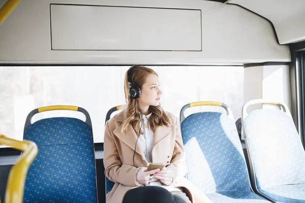 美しい幸せな若い女バスに座って 携帯電話を見て 音楽を聴くこと — ストック写真