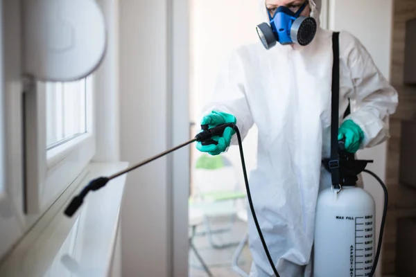 Exterminator in work wear spraying pesticide with sprayer
