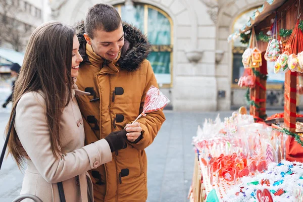Güzel genç çift birlikte City sokak, sarılma ve kalp şeklinde bir lolipop tutan zevk aşık. 