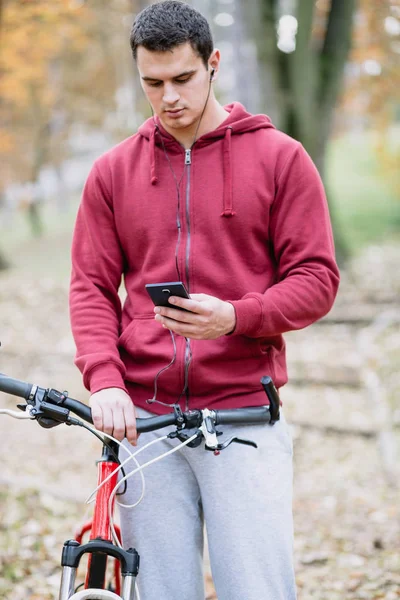 Sonbahar açık havada. Bisiklet Park ile ayakta, cep telefonu tutan kulaklık ile genç ciddi yakışıklı adam. Seçici odak.