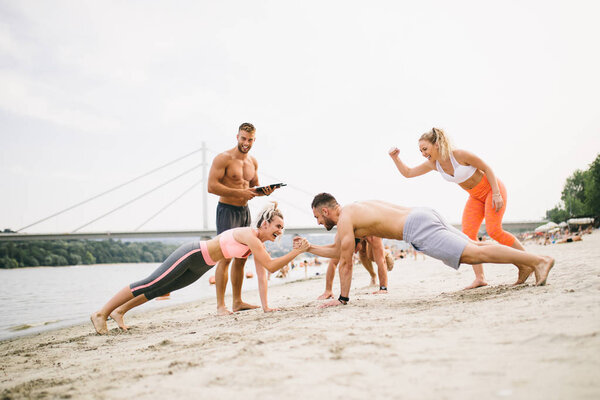 Group of young attractive people having fun at beach and doing some fitness workout.