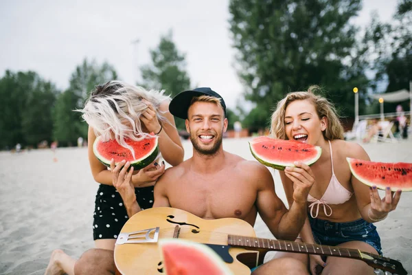 Young attractive man with two beautiful girls having fun while eating watermelon