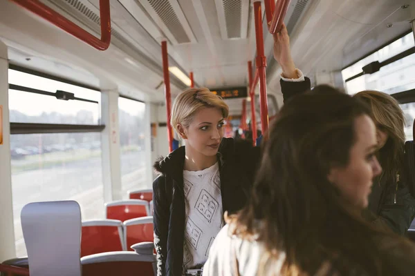 Three beautiful young women standing in tram, chatting and looking through windows.