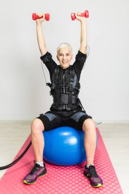 Güzel kadın kıdemli elektrik Kas stimülasyonu elbiseli egzersizleri yapıyor.