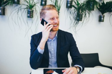 Cep telefonuyla konuşurken ve gülümseyen genç kendinden emin ve mutlu redhead iş adamı
