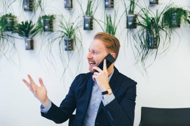 Cep telefonuyla konuşurken ve gülümseyen genç kendinden emin ve mutlu redhead iş adamı