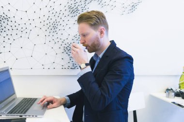 Kızıl saçlı Genç iş adamı laptop ya da defter üzerinde bir şey yapıyor ve kahve içme eller. Modern ofis iç. Çalışma insanlar kavramı.