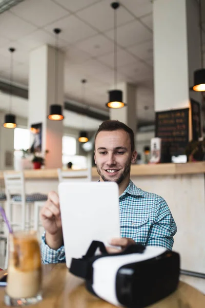 Young man sitting in cafe bar with virtual reality goggles