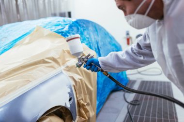 Koruyucu giysi ve sprey kompresör kullanarak maske resim araba olan adam. Seçici odak.