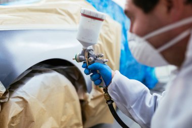 Koruyucu giysi ve sprey kompresör kullanarak maske resim araba olan adam. Seçici odak.