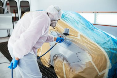 Koruyucu giysi ve sprey kompresör kullanarak maske resim araba olan adam. Seçici odak.